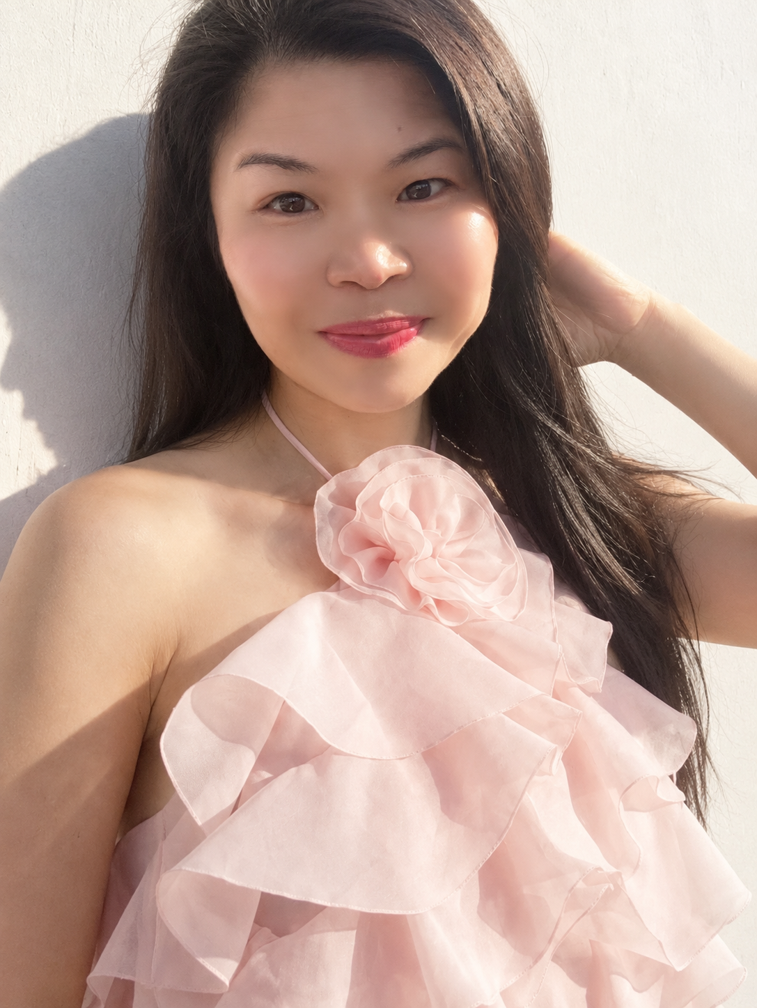 A woman in the ruffled pink halter crop top, photographed against a sunlit white wall